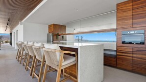 A modern kitchen with a bar area, wooden cabinets, and a view of the ocean. - Oceanview 2BR Near Beach + Golden Zone Rooftop (Bucerías)