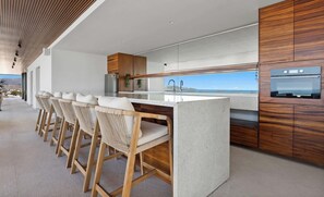 A modern kitchen with a bar area, wooden cabinets, and a view of the ocean. - Oceanview 2BR Near Beach + Golden Zone Rooftop (Bucerías)