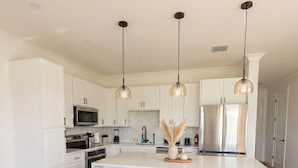 A modern kitchen with white cabinets, a central island with stools, stainless steel appliances, and pendant lighting. - Golf Course Living at Its Best 3BR Luxury Stay #1 (Punta Gorda)
