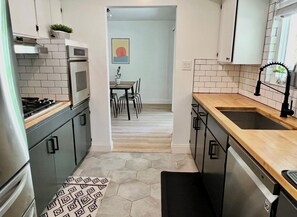 A narrow kitchen with a microwave, oven, and dishwasher. There is a dining area with a table and chairs visible through an open doorway. - Napa Home 10 Minutes from BottleRock & Downtown (Napa)
