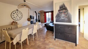 A dining area with a long table, chairs, a clock, a fireplace, and a large painting. - Charming gîte near Gourdon - stone, nature, enclosed garden, terrace (Concorès)