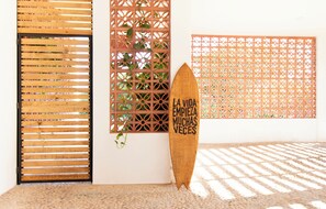 Une planche de surf en bois avec du texte, une porte en bois à lattes et un mur en treillis orné de plantes.
