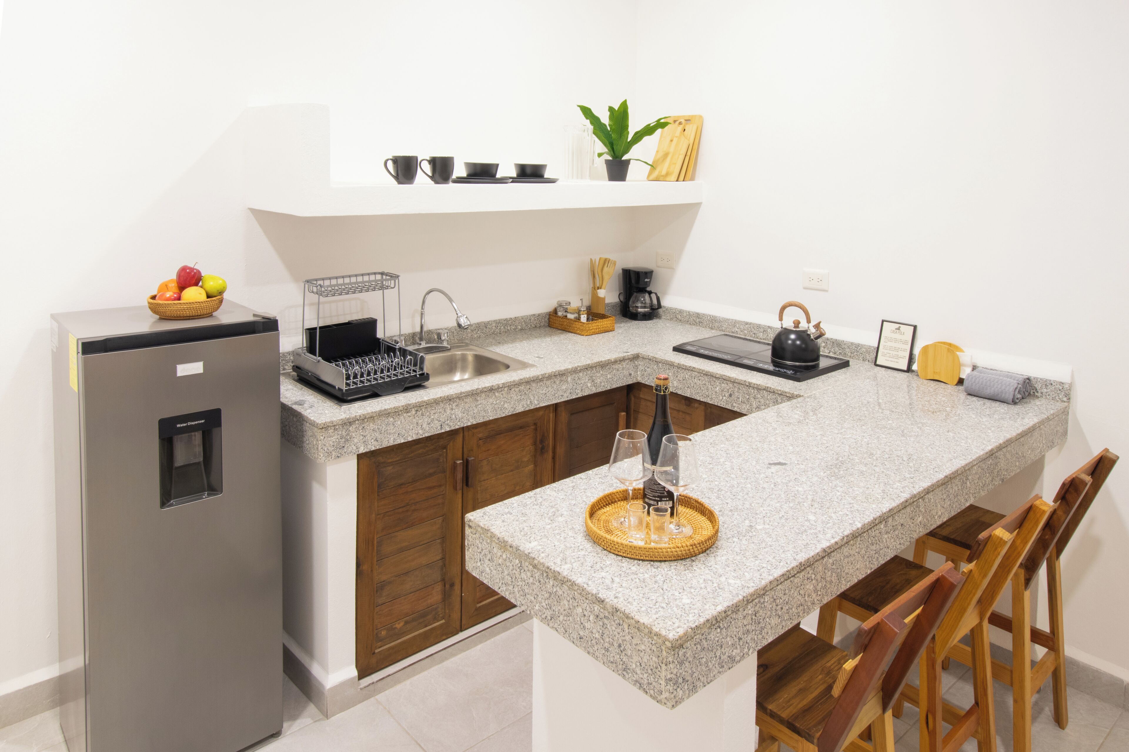 A kitchen with a granite countertop, wooden cabinets, a built-in sink, a refrigerator, and a bar area with stools.