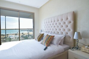 Une chambre avec un grand lit, deux coussins décoratifs, une lampe de chevet et une vue sur la plage.