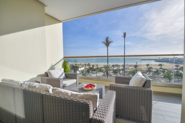 Un balcon doté de meubles en osier et offrant une vue sur la plage.