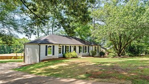 A single-story house with a covered porch, a front yard with grass, and trees.