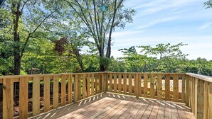 A wooden deck with a railing, surrounded by trees and greenery.