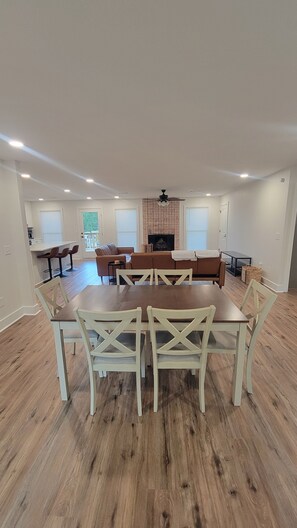 Amplia sala de estar con chimenea, comedor con mesa y sillas de madera y zona de cocina con taburetes de bar.