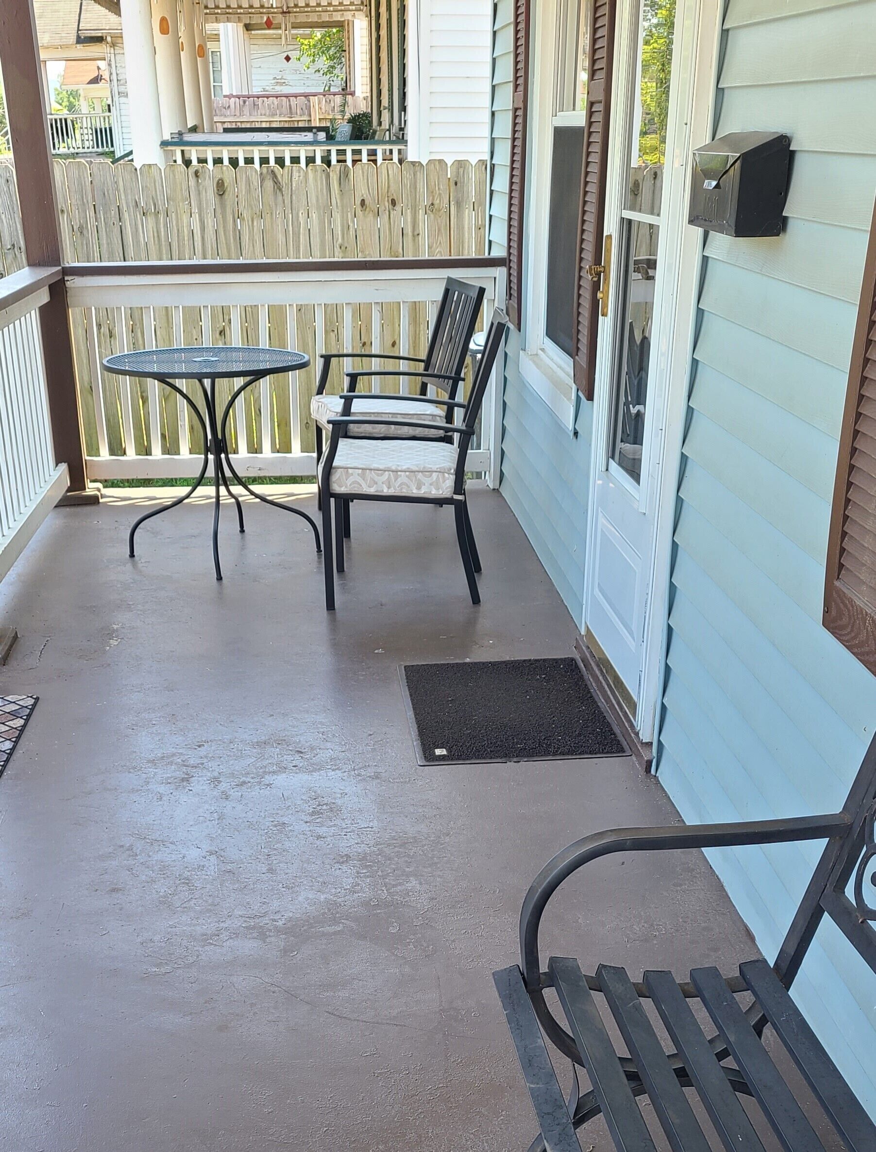 A covered porch with a metal table and two chairs, a wooden bench, and a mailbox on the wall.