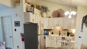 Een moderne keuken met witte kastjes, een roestvrijstalen koelkast en een eethoek met een ronde tafel en twee stoelen.