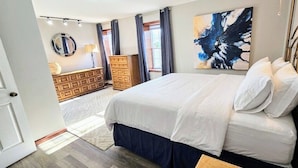 A bedroom with a bed, dresser, mirror, and abstract painting. - The off Main beach retreat! a spacious and cozy 6 bedroom home. (South Kingstown)
