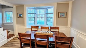 A dining room with a large table, six chairs, a bay window, and framed pictures on the walls. - The off Main beach retreat! a spacious and cozy 6 bedroom home. (South Kingstown)