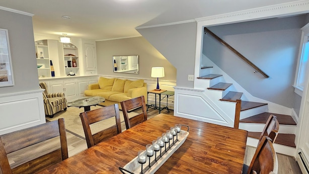 A dining area with a wooden table, chairs, and a tray with candles. A yellow sofa and a glass coffee table are in the background. - The off Main beach retreat! a spacious and cozy 6 bedroom home. (South Kingstown)