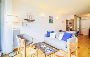 A living room with a sofa, chairs, a coffee table, a ship model, and a bookshelf. - L'Éscale Néréides : Vue Mer & Thalasso à pied (Bénodet)