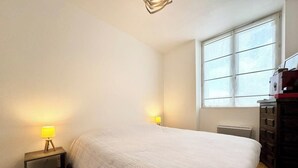 Ein Schlafzimmer mit einem Bett, zwei Nachttischlampen, einer Kommode und einem Fenster.