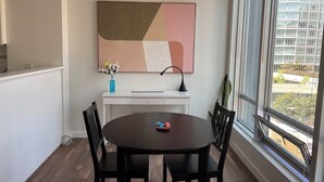 Een eethoek met een ronde tafel, stoelen, een vaas met bloemen en een groot abstract schilderij aan de muur.
