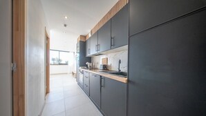 A modern kitchen with dark cabinets, a wooden countertop, and a view to the outside. - La Vie en Bleu : T3 Lumineux (Guidel)