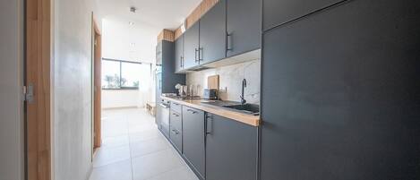 A modern kitchen with dark cabinets, a wooden countertop, and a view to the outside.