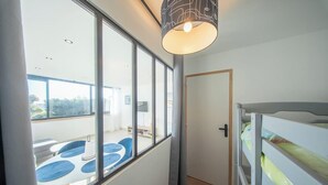 A room with a bunk bed, large windows, a ceiling light fixture, and a door. - La Vie en Bleu : T3 Lumineux (Guidel)