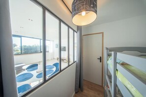 Ein Zimmer mit Etagenbett, großen Fenstern, einer Deckenleuchte und einer Tür.