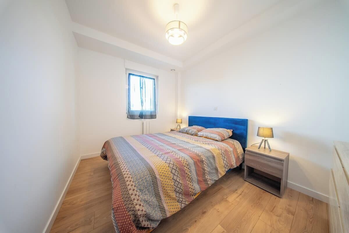 Ein Schlafzimmer mit einem Bett, Nachttischen, einem Fenster und einer Deckenleuchte.