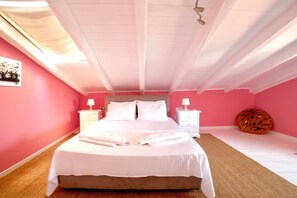 A bedroom with a large bed, two bedside tables, a round orange cushion, and a ceiling fan. - Oeve Apartment - A Colourful Loft in Kefalonia (Kefalonia)