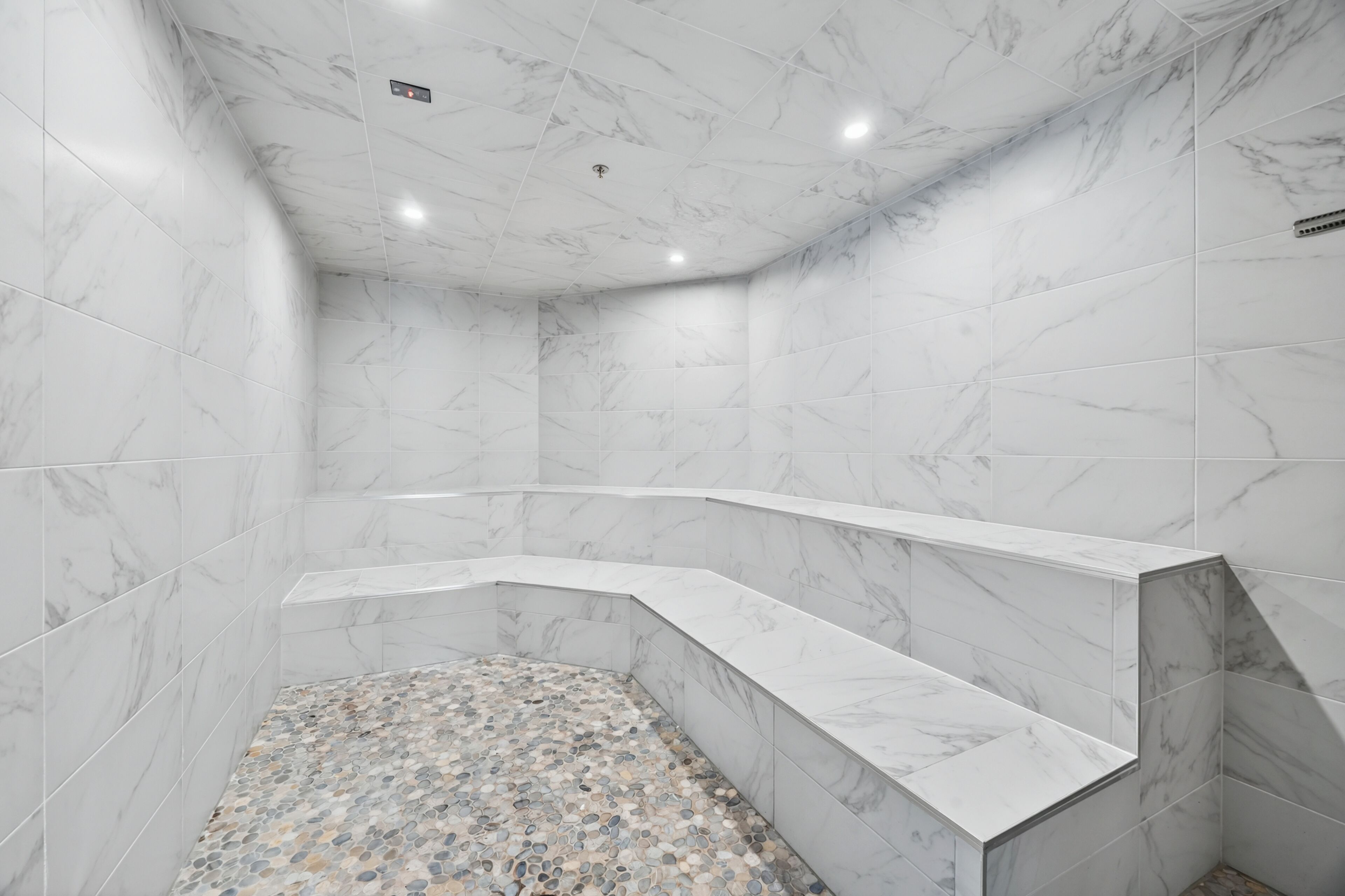 Une salle de bain moderne avec des murs en marbre, un sol à motifs de galets et un banc intégré.
