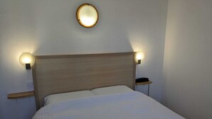 Una cama con cabecera de madera, dos lámparas de noche y una lámpara fijada a la pared.