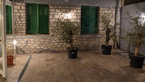 Un patio con paredes de piedra, contraventanas verdes, plantas en macetas y una lámpara.