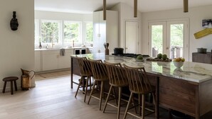 Une cuisine moderne dotée d’un grand îlot central, de chaises en bois et de luminaires suspendus.