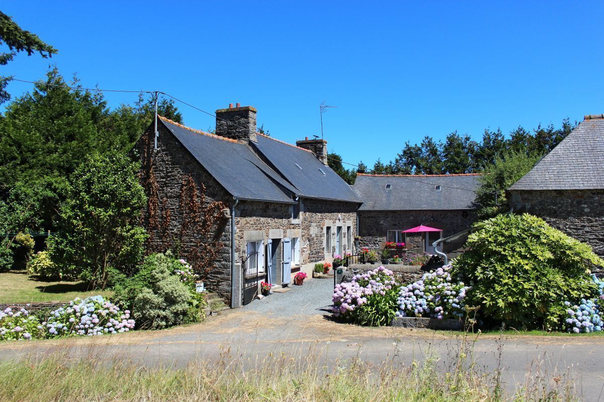 Ein Steinhaus mit einem geneigten Dach, einer gepflasterten Auffahrt und einem Garten mit Blumen.