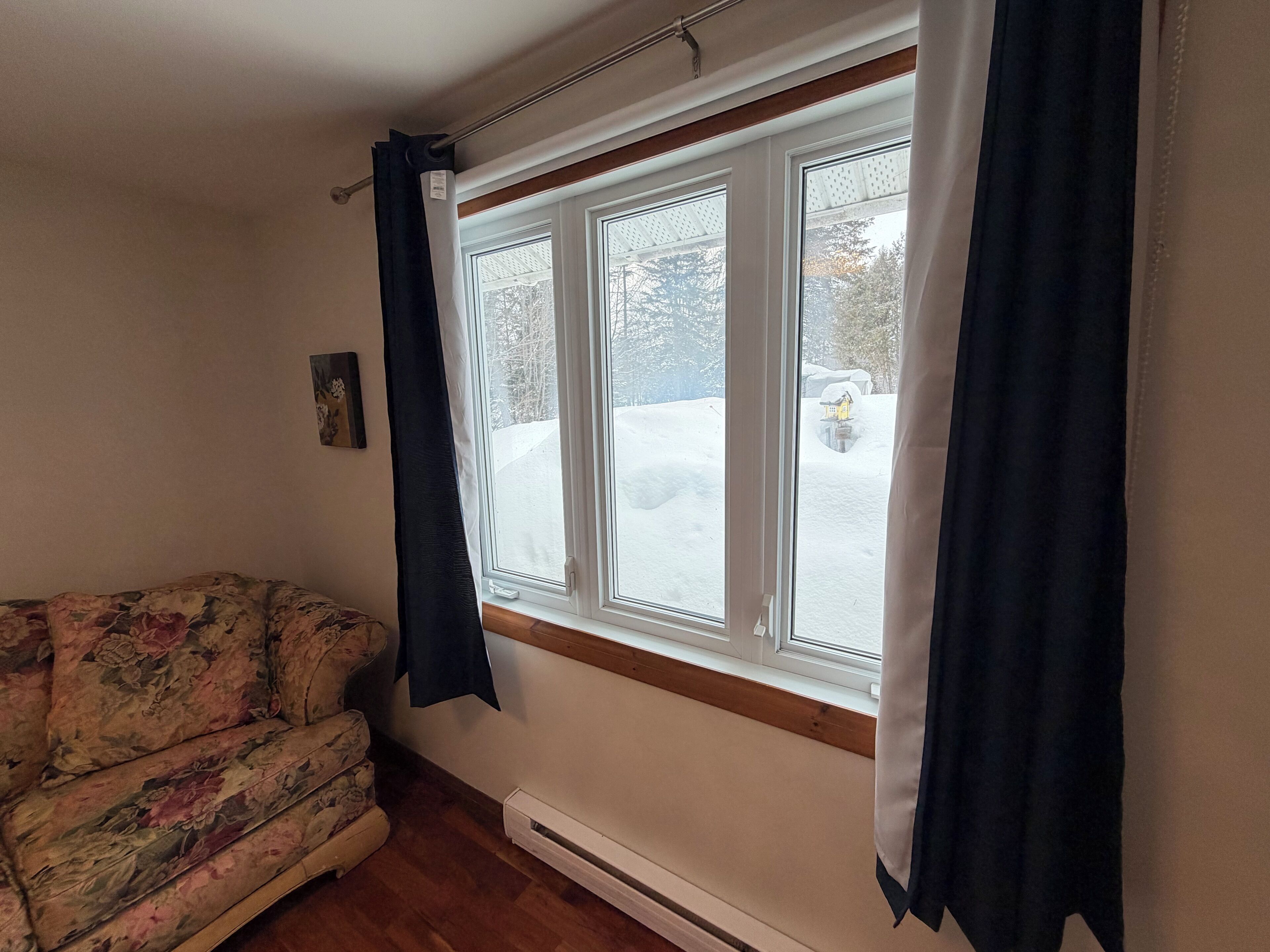 A room with a floral sofa, a radiator, and a window with curtains.