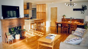A modern living room with a fireplace, wooden furniture, a dining area, and a kitchen in the background.