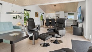 A modern living room with a sofa, chairs, a dining area, and a kitchen in the background.