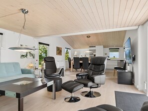 Ein modernes Wohnzimmer mit Sofa, Sesseln, einem Essbereich und einer Küche im Hintergrund.