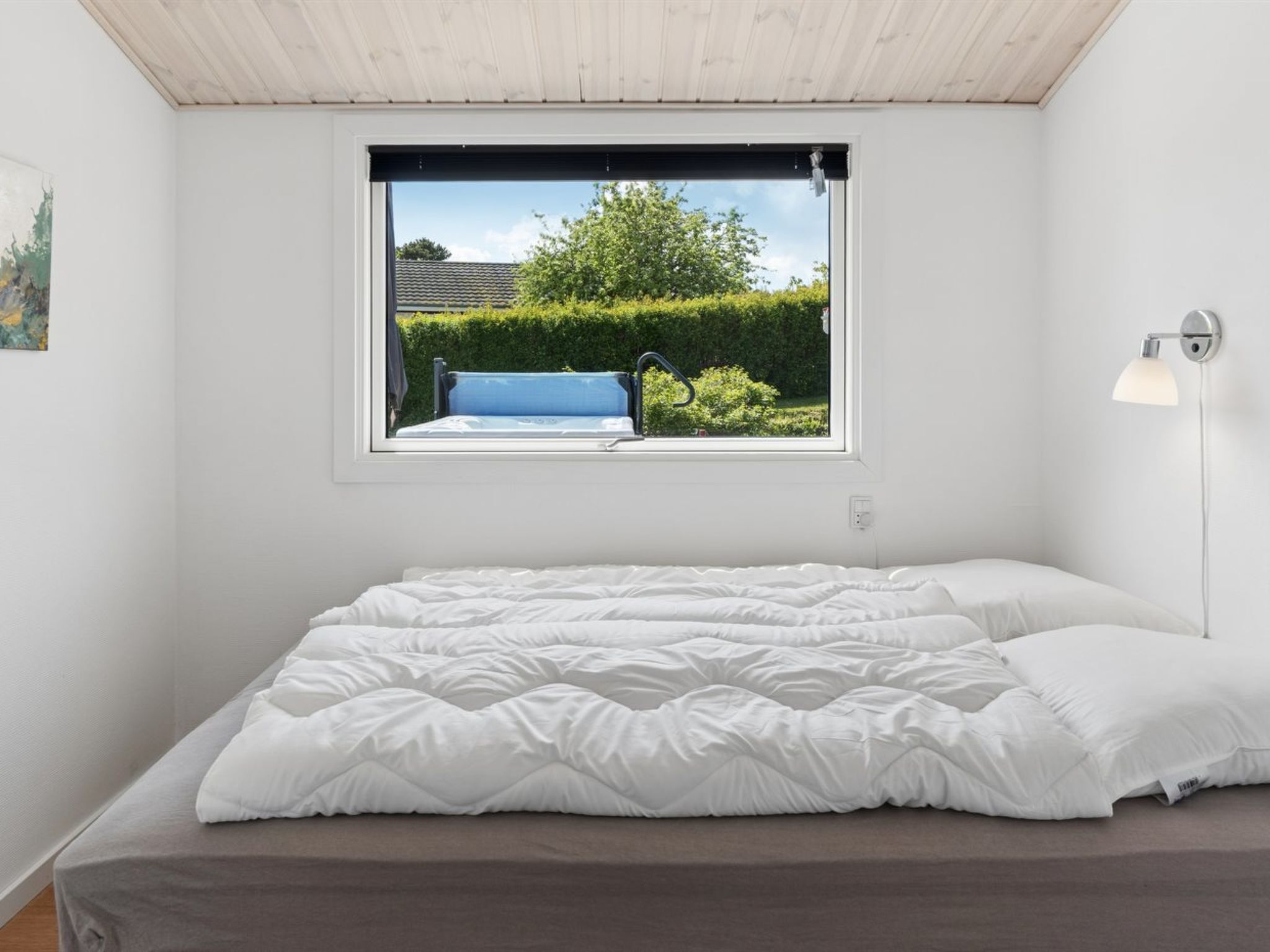 A bedroom with a bed, a window, and a wall-mounted lamp.