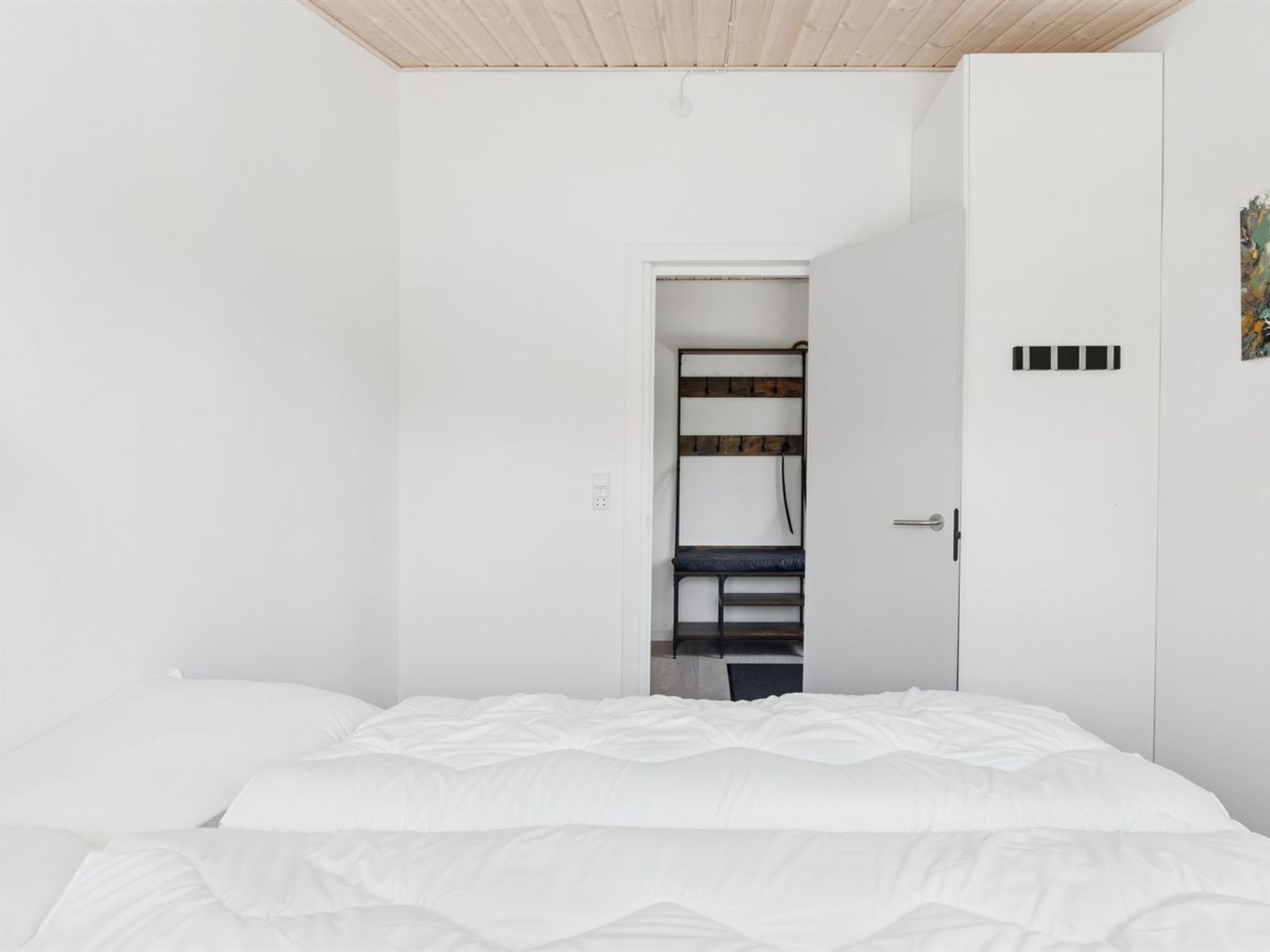 Et soveværelse med seng, garderobe og bænk med kroge.