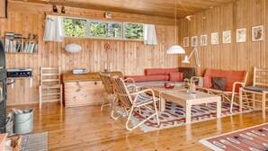 En stuga med träpanel på insidan, inredd med en soffa, stolar, ett bord och en öppen spis.