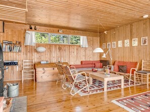 Interior de una cabaña de madera con sofá, sillas, una mesa y chimenea.