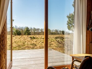 Una habitación con un ventanal grande, una terraza de madera y vistas a un campo cubierto de hierba.