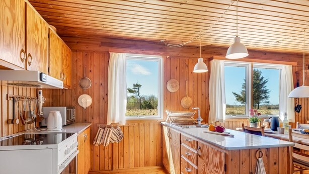 En stuga byggd av trä med kök, matplats och stora fönster.