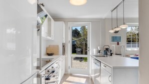 Moderni keittiö, jossa on valkoiset kaapit, sisäänrakennettu uuni ja suuri keittiösaareke, jossa on pesuallas.