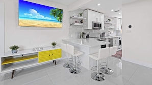 A modern kitchen with white cabinets, a central island with bar stools, a microwave, and a washing machine. - Walk to Las Olas - Modern Apt w/ Fast WiFi (Fort Lauderdale)