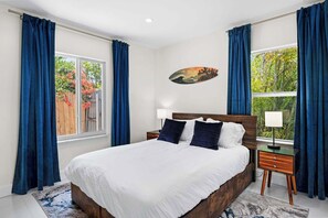 A bedroom with a large bed, two bedside tables, a window with curtains, and a painting on the wall. - Walk to Las Olas - Modern Apt w/ Fast WiFi (Fort Lauderdale)
