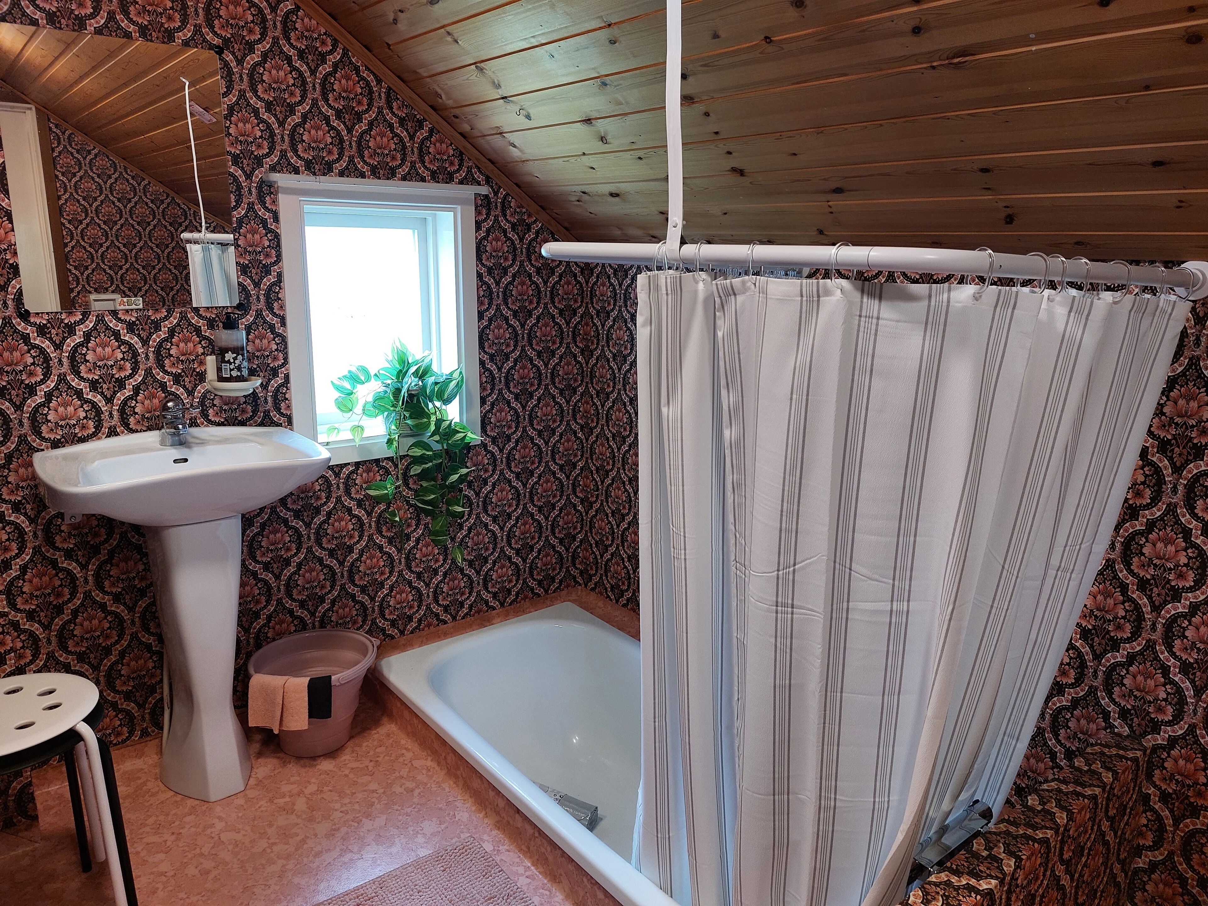 A bathroom with a sink, window, shower curtain, and patterned wallpaper.