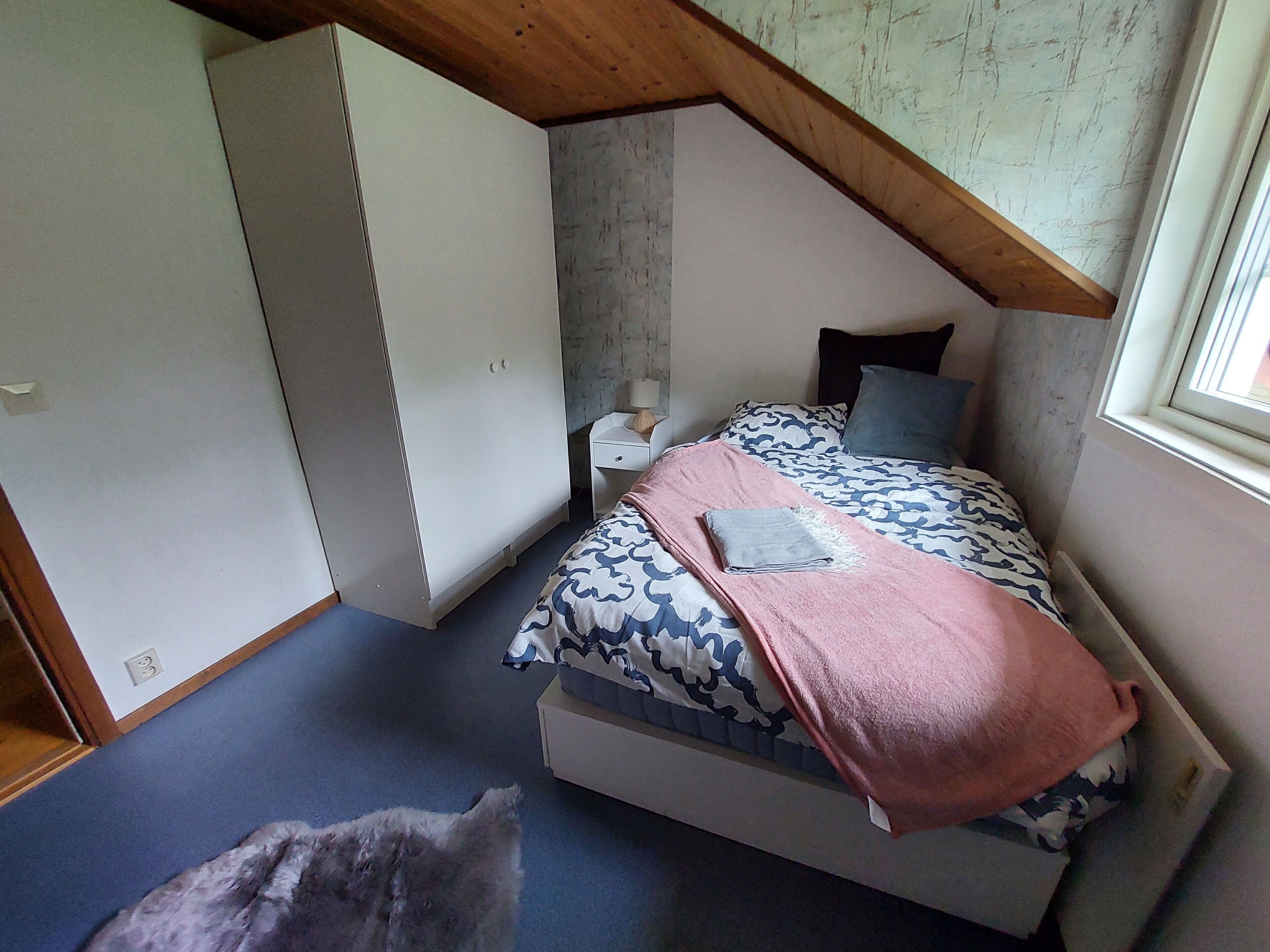 A bedroom with a bed, a nightstand, a wardrobe, and a window.