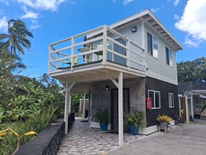 A two-story building with a balcony, potted plants, and a pathway leading to the entrance. - Two houses for the price of one at beautiful orchid farm. (Pāhoa)