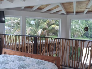 Ein Schlafzimmer mit Bett, Holz-Kopfteil und einem Balkon mit Blick auf Palmen.