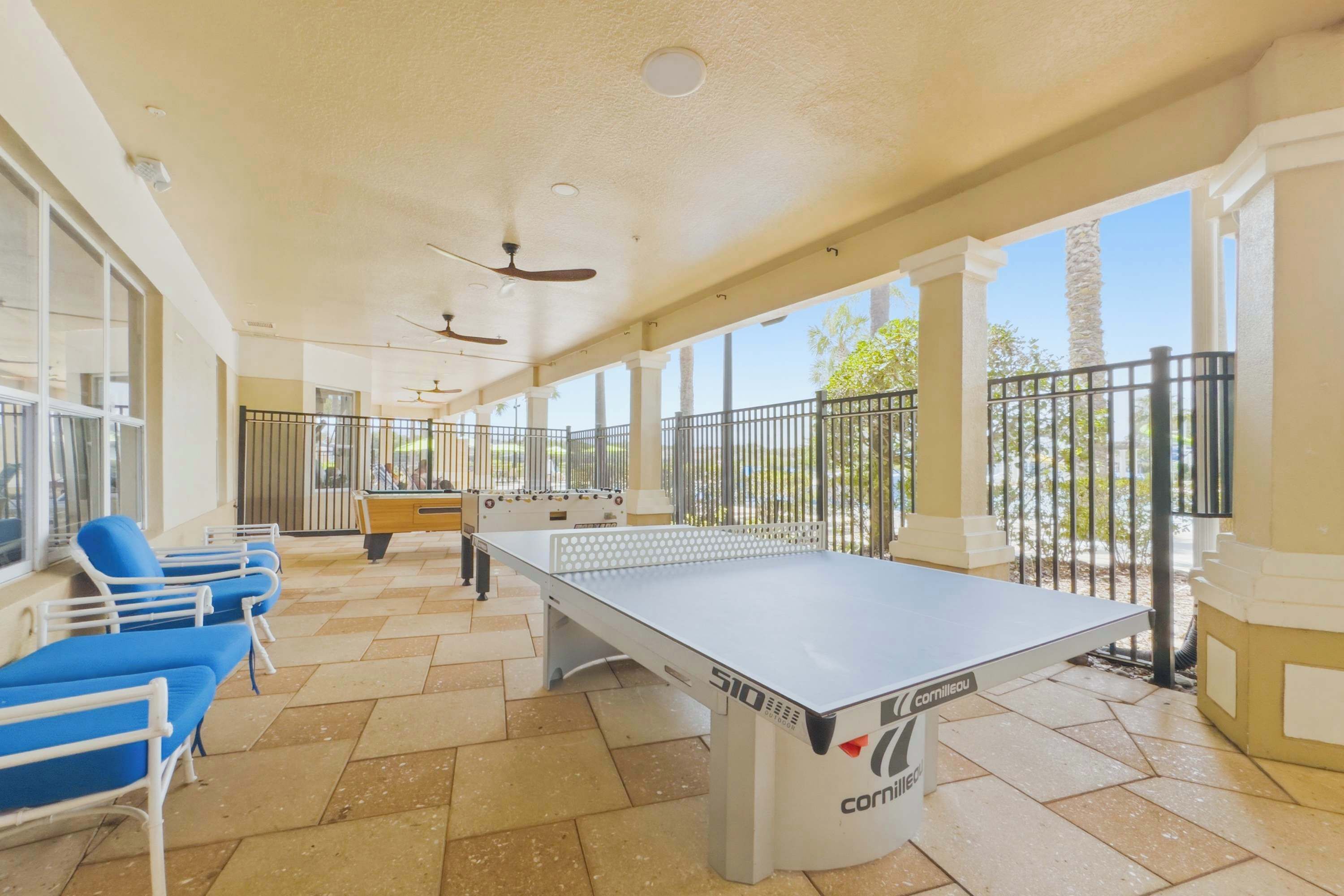 A covered outdoor area with a foosball table, blue lounge chairs, and a pool table.