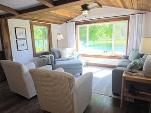Una sala de estar acogedora con un sofá, sillones y un ventanal con vistas a un lago.